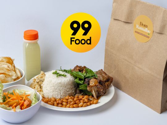 Prato com arroz, feijão, carne, salada e acompanhamentos ao lado da embalagem do Dom Ramalho e da marca 99Food